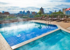 Vista de uma piscina aquecida em um dos hotéis com piscina aquecida em Foz do Iguaçu, com espreguiçadeiras ao redor e uma bela paisagem urbana ao fundo, oferecendo relaxamento e conforto para os hóspedes.