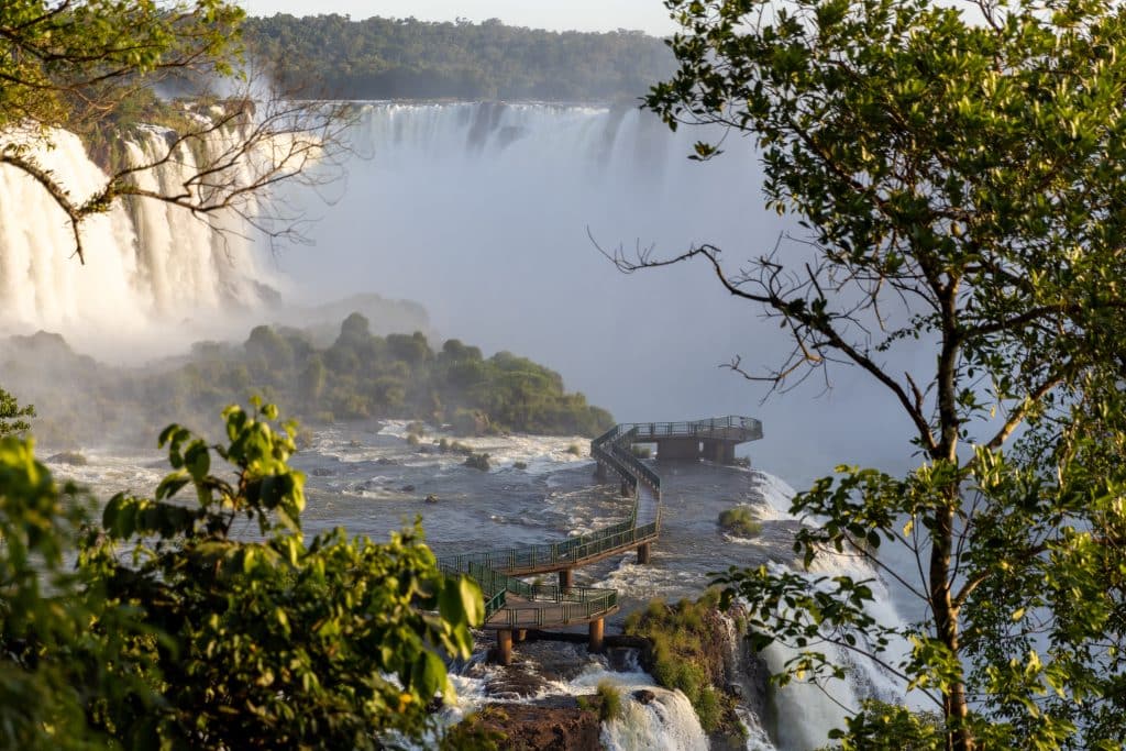 Vista panorâmica das Cataratas do Iguaçu com passarela sobre o rio, cercada por vegetação exuberante, destacando uma das principais atrações turísticas de Foz do Iguaçu.