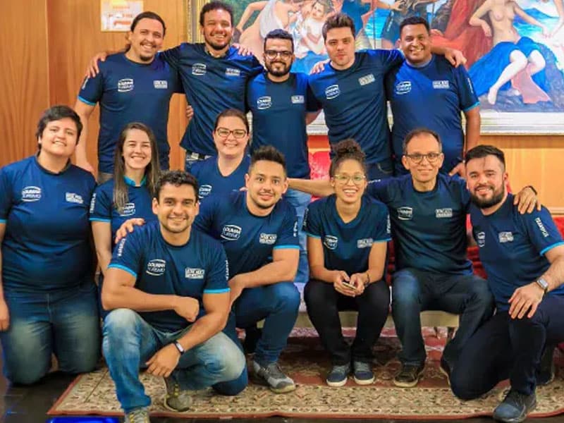 Equipe de colaboradores da Loumar Turismo, usando camisetas azuis com o logotipo da empresa, posando em ambiente interno decorado com obras de arte.