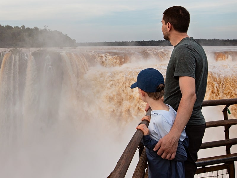 Pai e filho admirando a impressionante vista das Cataratas do Iguaçu, um dos principais pontos turísticos ao viajar com crianças para Foz do Iguaçu.