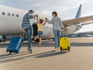 Família feliz com malas de viagem, incluindo uma criança sendo levantada pelos pais, caminhando em direção a um avião. Eles estão prontos para viajar com crianças para Foz do Iguaçu.