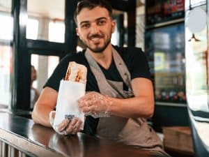 Homem sorridente segurando shawarma fresco em uma lanchonete, representando uma ótima opção para quem busca onde comer shawarma em Foz do Iguaçu