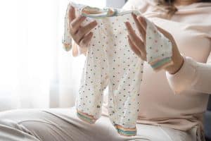 Mulher segurando um macacão de bebê com estampa de bolinhas coloridas. Descubra onde comprar roupas de bebê no Paraguai para encontrar peças adoráveis e confortáveis.