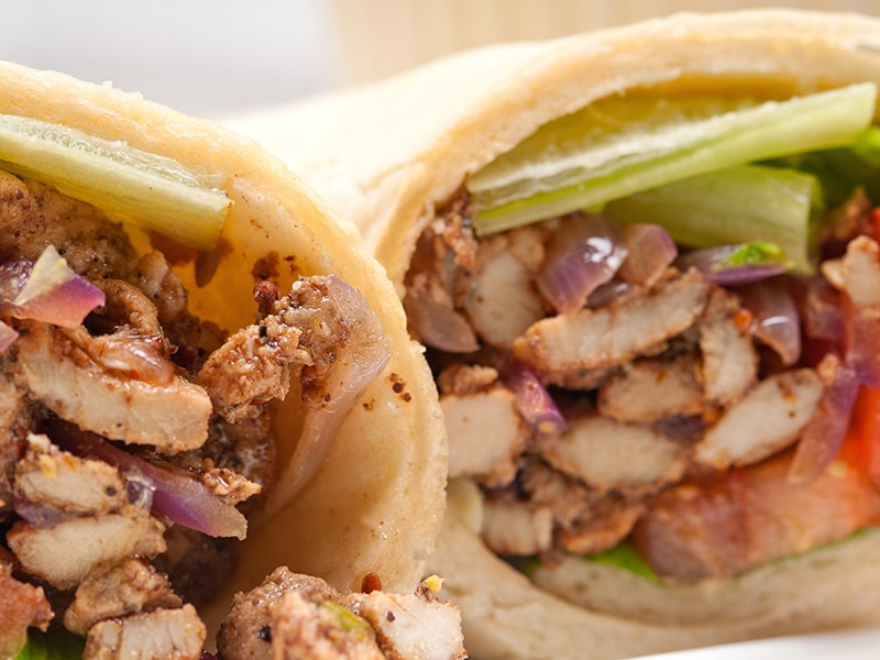 Close-up de um shawarma recheado com carne temperada, cebolas, pimentão e alface, mostrando detalhes dos ingredientes frescos e saborosos.