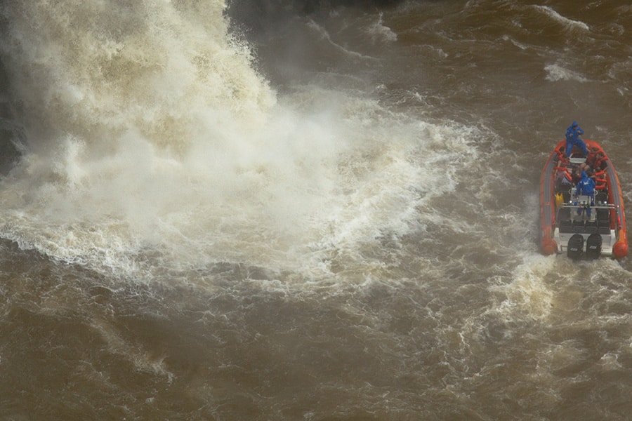 Macuco Safari leva turistas para perto de uma impressionante queda d'água nas Cataratas do Iguaçu, com a força da água criando uma névoa ao redor.