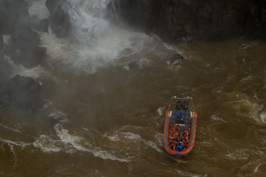 Vista aérea de um barco do Macuco Safari navegando pelas águas turbulentas próximas às Cataratas do Iguaçu, com turistas prontos para se aventurar.