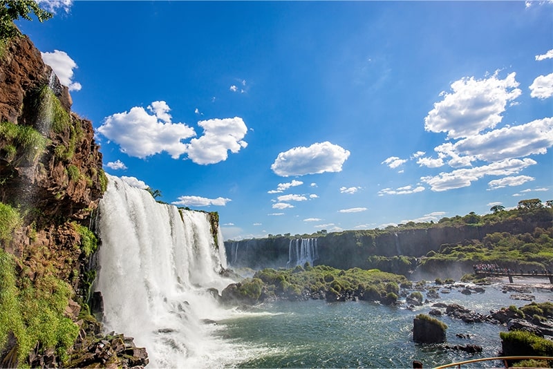 Cataratas do Iguaçu em um dia ensolarado, com cascatas de água caindo sobre rochas e vegetação exuberante ao redor, um destino perfeito para viajar no fim do ano e aproveitar a beleza natural e tranquilidade do lugar.