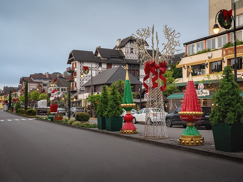 Rua decorada para o Natal em uma cidade com arquitetura de estilo europeu, com enfeites coloridos de árvores e figuras de Papai Noel ao longo da calçada, proporcionando uma atmosfera festiva e acolhedora.