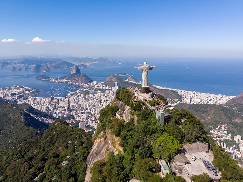 Vista aérea do Cristo Redentor no Rio de Janeiro, com a Baía de Guanabara e o Pão de Açúcar ao fundo, um dos destinos mais procurados para viajar no fim do ano, oferecendo paisagens deslumbrantes e uma experiência cultural única.